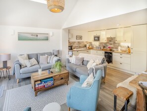 A modern living room with two sofas, a coffee table, and a dining area with a table and chairs. - Red Squirrel Cottage (Whitwell, near Ventnor)