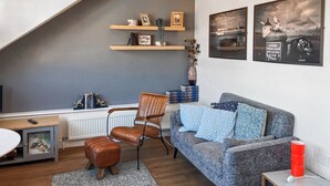Een moderne woonkamer met een loft-plafond, een grijze bank, een bruine leren fauteuil en een tafeltje met een rode vaas.