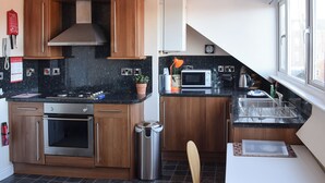 Een moderne keuken met houten kastjes, een roestvrijstalen oven, een magnetron en een kleine eethoek met uitzicht op een raam.