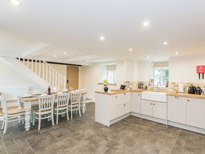 A modern kitchen with white cabinetry, a wooden staircase, and a dining area with white chairs.