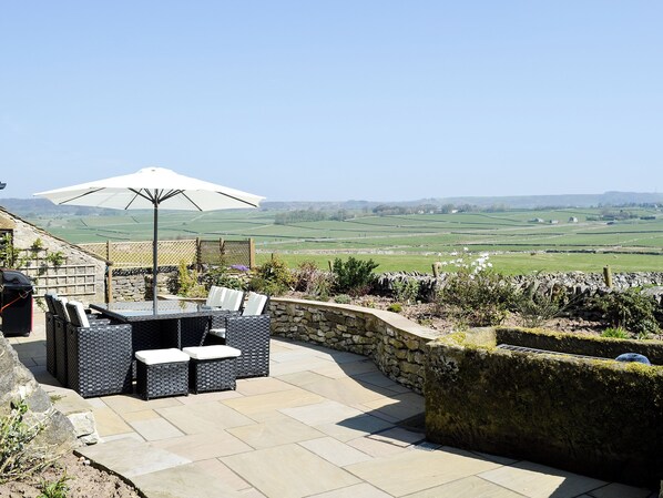 An outdoor patio with a table and chairs, a grill, and a view of the countryside.