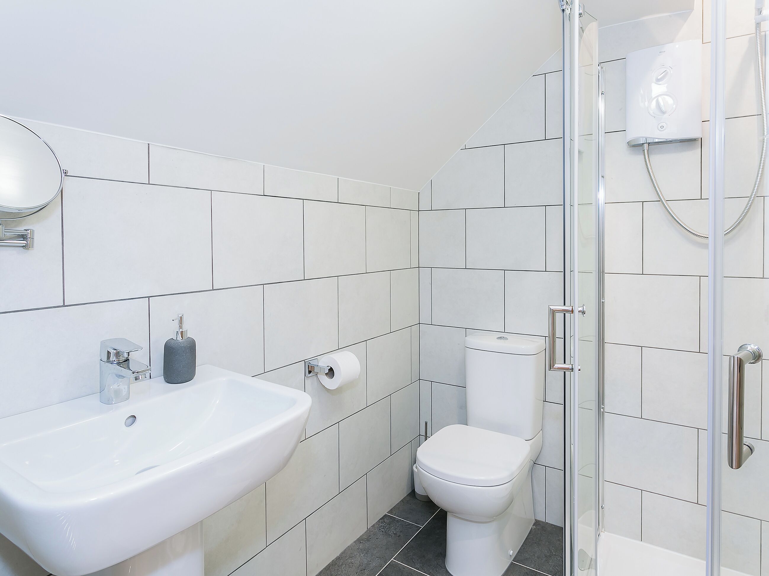 A bathroom with a white sink, toilet, and shower enclosure.