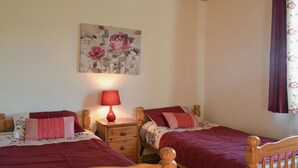 Un dormitorio con dos camas de madera, una mesita de noche, una lámpara roja y un cuadro con motivos florales en la pared.