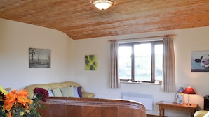 Una sala de estar acogedora con un sofá de cuero marrón, techo de madera y una ventana con cortinas.