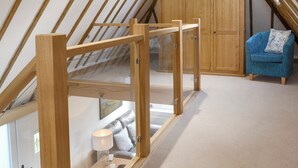 A room with a sloped ceiling, wooden beams, a glass door, a wooden wardrobe, a blue armchair, and a small table with a lamp. - 1 bedroom accommodation in Brede, near Rye (Brede, near Rye)