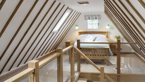 A bedroom with a sloped ceiling, wooden beams, a bed, a window, and a nightstand with a lamp. - 1 bedroom accommodation in Brede, near Rye (Brede, near Rye)