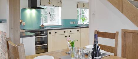Un coin repas avec une table en bois dressée pour deux personnes, une cuisine en arrière-plan et un escalier.