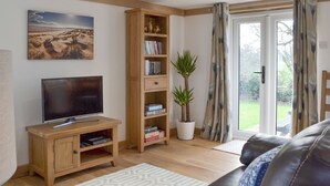 A living room with a flat-screen TV, wooden shelving, a potted plant, and a sliding glass door leading outside. - 1 bedroom accommodation in Brede, near Rye (Brede, near Rye)