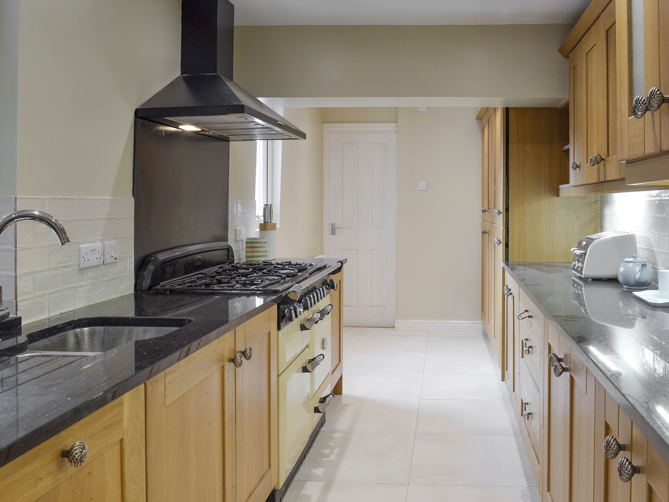 A kitchen with wooden cabinets, a black stove, and a stainless steel sink.
