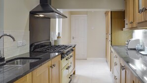 A kitchen with wooden cabinets, a black stove, and a stainless steel sink. - 3 bedroom accommodation in Bakewell (Bakewell)