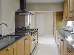 A kitchen with wooden cabinets, a black stove, and a stainless steel sink. - 3 bedroom accommodation in Bakewell (Bakewell)