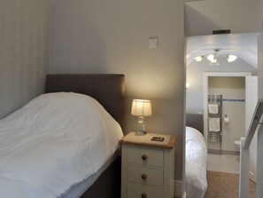 A neatly made bed with white linens, a bedside lamp, and a small wooden nightstand with drawers.