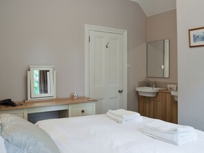 A bedroom with a bed, a bedside table with a lamp, a dresser, a mirror, and a bathroom with a sink and mirror.