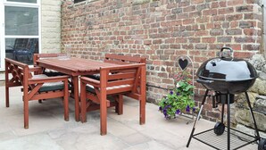 A patio with a wooden table and chairs, a barbecue grill, and a brick wall. - 3 bedroom accommodation in Bakewell (Bakewell)