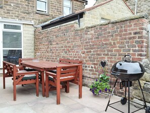 A patio with a wooden table and chairs, a barbecue grill, and a brick wall.