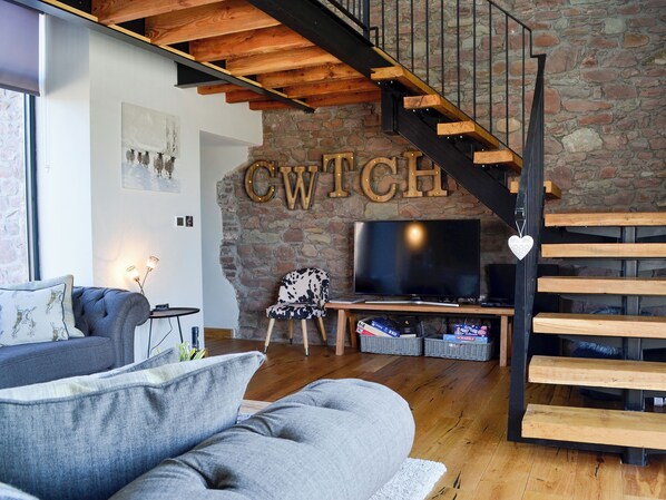 A modern living room with a stone wall, a television, and a wooden staircase.