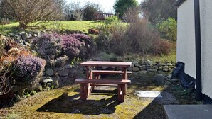 Una mesa de picnic en un jardín con un muro de piedra y diversas plantas.
