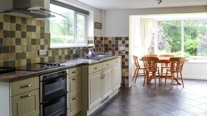 Een keuken met een groot eiland, donkere betegelde vloer en een eethoek met tafel en stoelen.