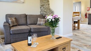 En stue med en grå sofa, et træbord, en vinflaske og en vase med blomster.