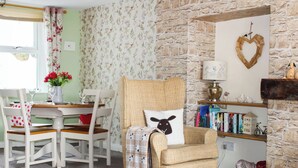 A cozy room with a wicker armchair, a dining table with chairs, a bookshelf, and a stone wall. - 2 bedroom accommodation in Loftus, near Saltburn-by-the-Sea (Loftus, near Saltburn-by-the-Sea)