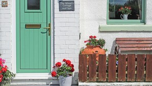 A green door with a small window, a sign reading "The Miner's Cottage", and a wooden fence with potted plants. - 2 bedroom accommodation in Loftus, near Saltburn-by-the-Sea (Loftus, near Saltburn-by-the-Sea)