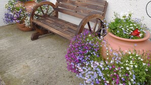 A wooden bench with a wheel backrest, placed on a concrete surface next to two large terracotta pots filled with flowers. - 2 bedroom accommodation in Loftus, near Saltburn-by-the-Sea (Loftus, near Saltburn-by-the-Sea)