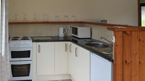 Une cuisine de taille réduite, avec des meubles blancs, une cuisinière, un four, un four à micro-ondes et un évier.