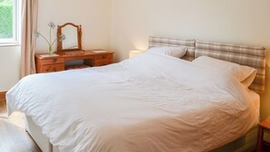 Un lit bien fait, avec une tête de lit, une commode en bois avec un miroir et une fenêtre avec des rideaux.