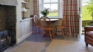 A cozy room with a fireplace, a dining table with chairs, and a window with plaid curtains. - 2 bedroom accommodation in Burtersett, near Hawes (Burtersett, near Hawes)