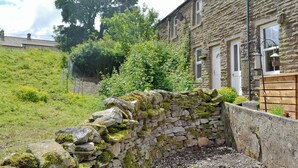 A stone wall with moss, a garden with various plants, and a stone building with windows and a door. - 2 bedroom accommodation in Burtersett, near Hawes (Burtersett, near Hawes)