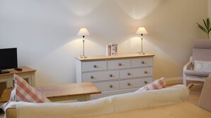 Una habitación con una cama, una silla, una mesita pequeña, un aparador con cajones y dos lámparas de pared.
