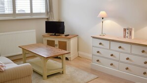 Una habitación con una mesa de madera, un televisor sobre un mueble, una lámpara y un aparador con cajones.