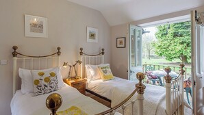 Une chambre avec deux lits, une table de chevet en bois, une fenêtre donnant sur l’extérieur et un balcon aménagé avec du mobilier d’extérieur.
