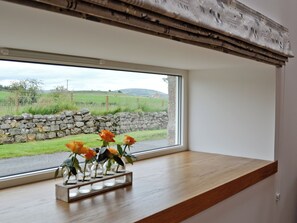 A window with a view of a stone wall and a grassy field.