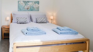 Ein ordentlich bezogenes Bett mit zwei Kissen, ein Nachttisch mit einer Lampe und ein Gemälde an der Wand.