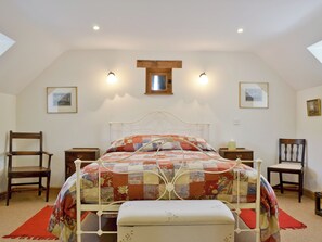 A bedroom with a metal bed frame, a quilted bedspread, two bedside tables, a wooden chair, and a small wooden cabinet.