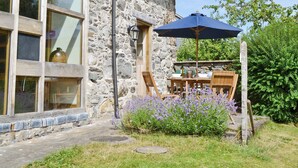 A stone building with a patio table and chairs, a blue umbrella, and purple flowers. - 3 bedroom accommodation in Pedairffordd (Pedairffordd)