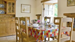 A dining area with wooden chairs, a table with a checkered tablecloth, and a window with a view of greenery. - 3 bedroom accommodation in Pedairffordd (Pedairffordd)