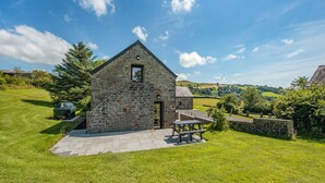Ein Steinhaus mit kleinem Fenster, einer gepflasterten Terrasse und einem Picknicktisch.