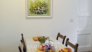 Una mesa de comedor con mantel a cuadros, un cuadro de flores en la pared y una porción de pastel en un plato.