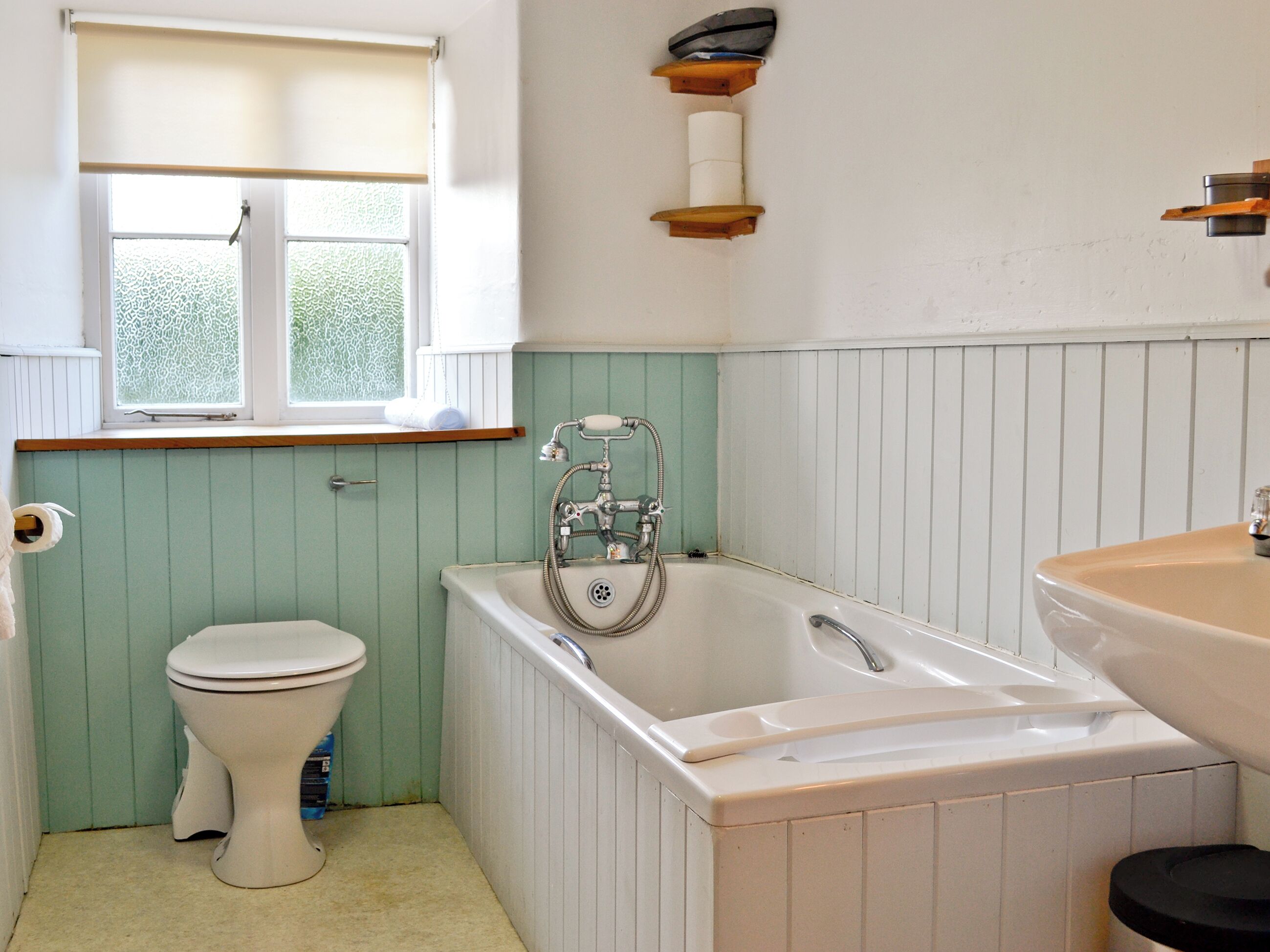 A bathroom with a toilet, a bathtub, a sink, a window with a blind, and a towel rack.