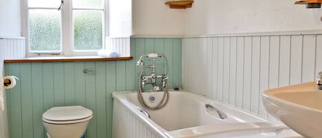 A bathroom with a toilet, a bathtub, a sink, a window with a blind, and a towel rack.