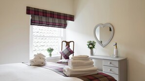 A bedroom with a bed, a dresser, a mirror, and a window with a plaid valance.