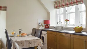 A kitchen with a dining table, a washing machine, a sink, and a window with a plaid valance.