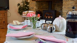 Un comedor acogedor con chimenea de piedra, un televisor y una mesa dispuesta con tazas de té, tetera y pastel.