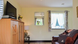 A living room with a brown leather sofa, a wooden cabinet, a TV, and a window with curtains. - Hunter's Cottage - UK6239 (Y Ff&ocirc;r, near Pwllheli)