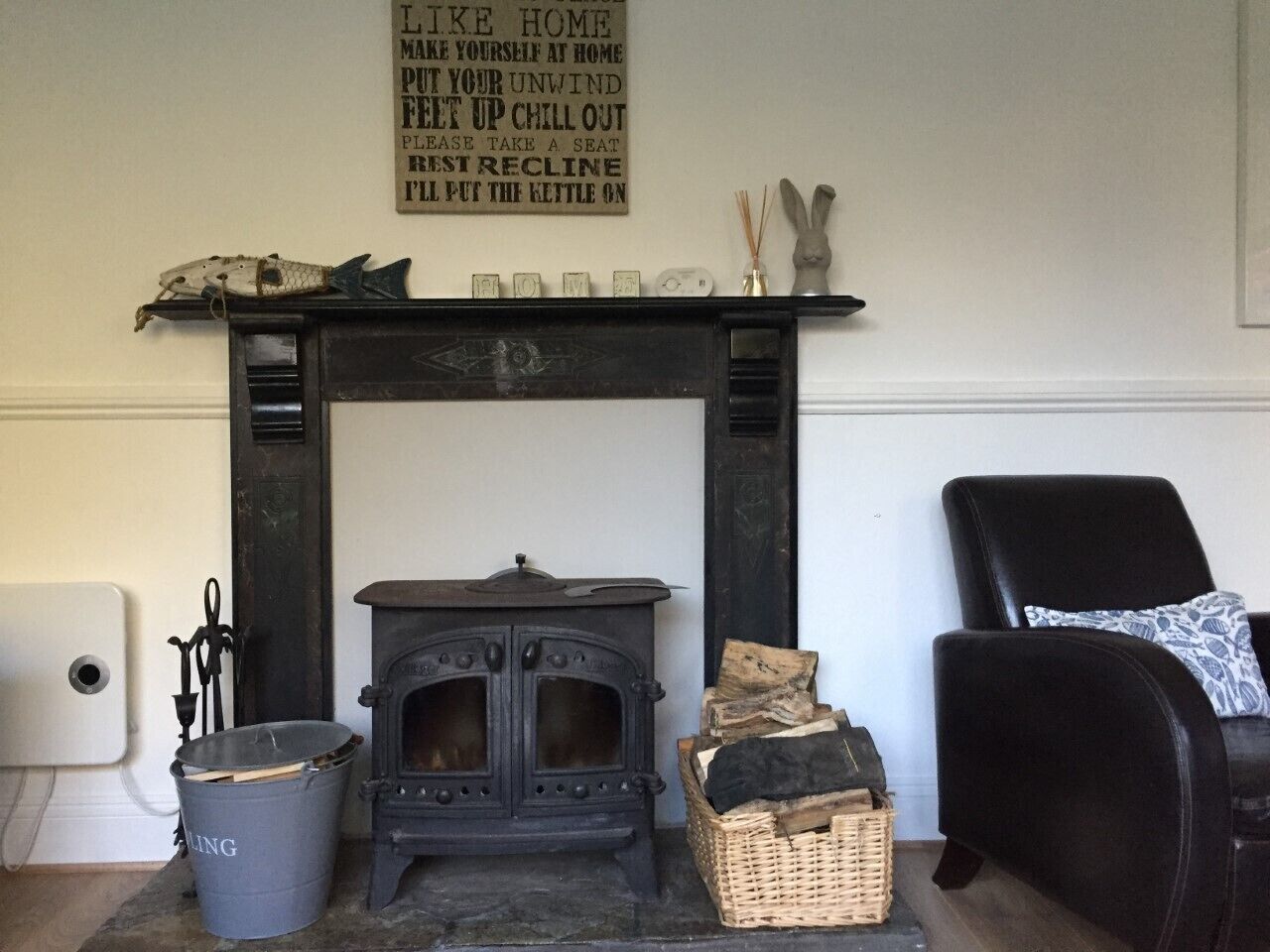A traditional fireplace with a sign above it, a black chair, a wicker basket, and a grey bucket.