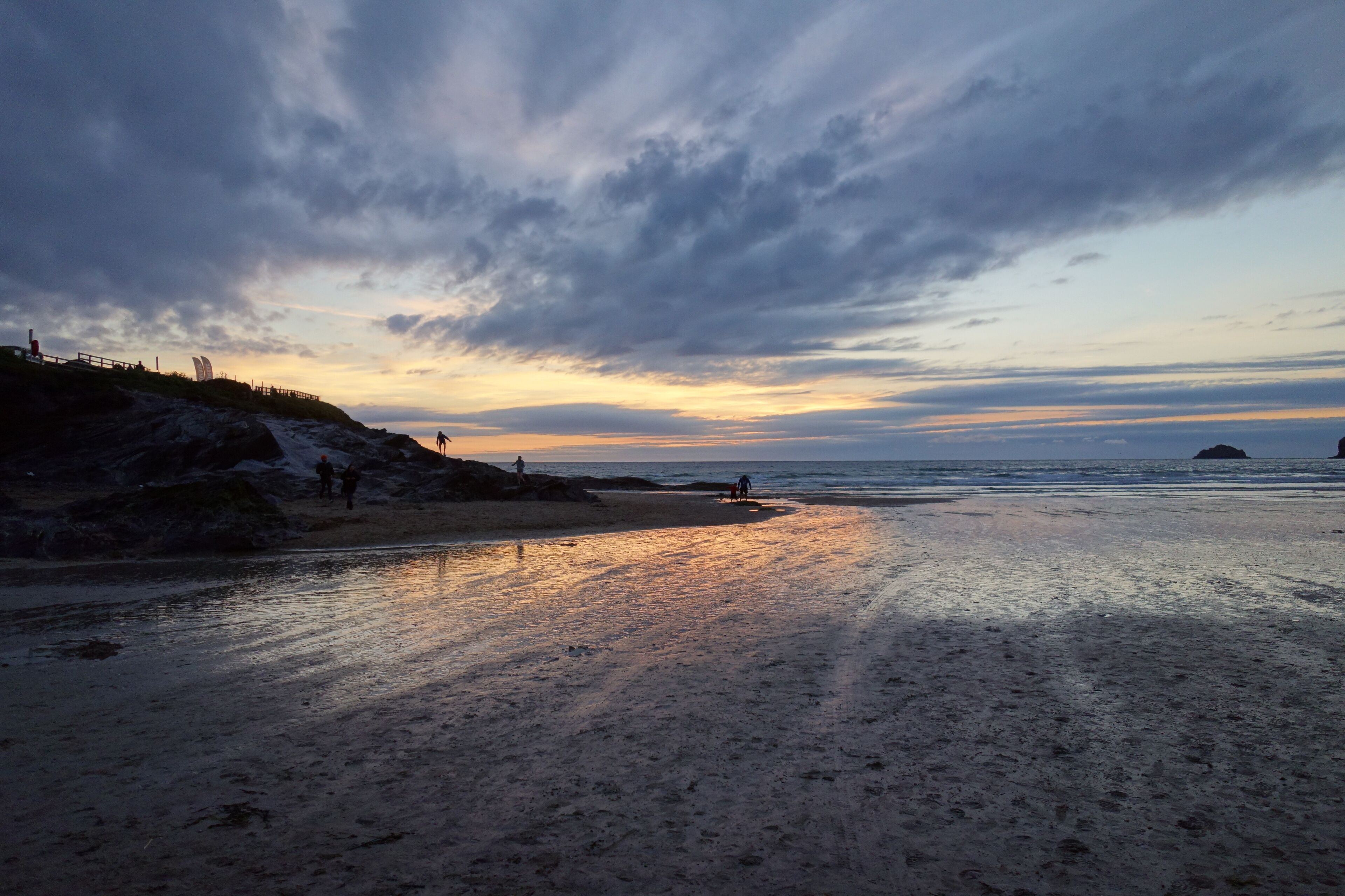 A beach with a rocky shoreline and a few people walking.
