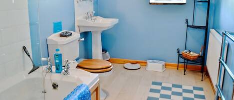 A bathroom with a toilet, sink, bathtub, and a shelf with toiletries.