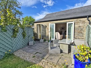 A stone house with a patio, wicker furniture, and a blue planter. - 2 bedroom accommodation in Three Crosses, Gower, Swansea (Three Crosses, Gower, Swansea)